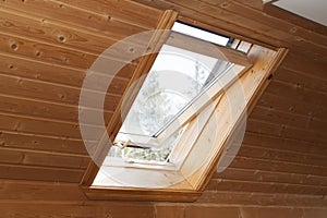 Open dormer window in wooden house in the attic. Room has sloping ceiling made of natural eco-materials and views of park through