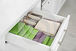 Open drawer with different folded towels and napkins in kitchen