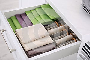 Open drawer with different folded towels and napkins in kitchen, closeup