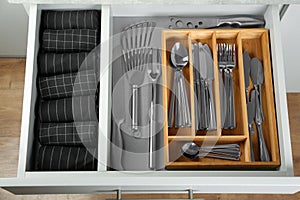 Open drawer with different utensils and folded towels. Order in kitchen