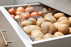 Open drawer with potatoes and onions. Orderly storage