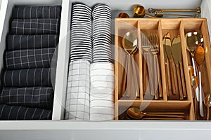 Open drawer with utensils and folded towels. Order in kitchen