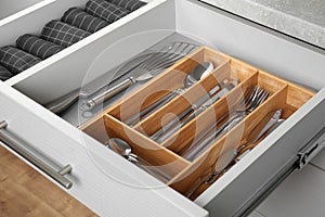 Open drawer with utensils and folded towels. Order in kitchen