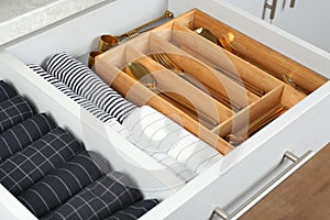 Open drawer with utensils and folded towels. Order in kitchen