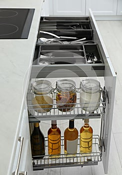 Open drawers with jars of food, wine bottles and utensils in kitchen