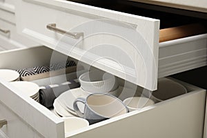 Open drawers of kitchen cabinet with different dishware and towels