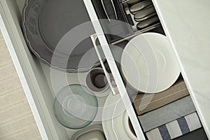 Open drawers of kitchen cabinet with different dishware and towels, top view