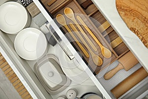 Open drawers of kitchen cabinet with different dishware and utensils, top view