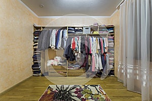 Open dressing closet wardrobe full of different male and female colorful clothes and accessories on hangers and shelf. Modern