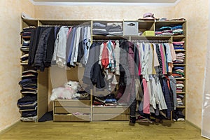 Open dressing closet wardrobe full of different male and female colorful clothes and accessories on hangers and shelf. Modern