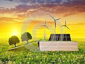 Open ecological book with solar panel and wind turbine on meadow at sunset.