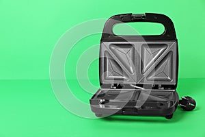 Open electric sandwich maker on green background, space for text