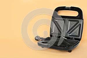 Open electric sandwich maker on pale orange background, space for text