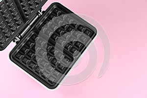 Open electric waffle maker on pink background, top view. Space for text