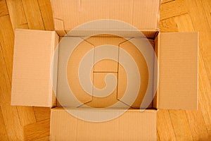 Open empty cardboard parcel on the wooden parquet floor