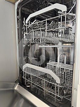 Open empty dishwasher with clean metal racks in a modern kitchen setting. Home Cleaning Routine