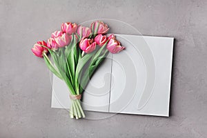 Open empty notebook and bouquet of pink tulip flowers on gray stone table top view in flat lay style. Woman working desk.