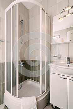 Open empty shower stall and washbasin in the bathroom with white tiles.