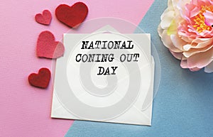 An open envelope with the text NATIONAL Coning Out DAY, on a pink and blue background with a decor of felt hearts and a flower.