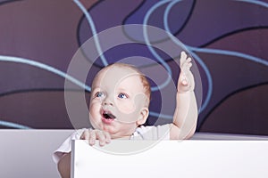 Open-eyed baby boy in his bed. Open-mouthed blue-eyed infant kid in a crib