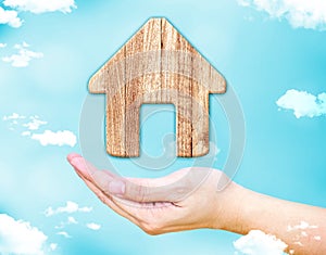 Open female hand with Home wood icon with blue sky and cloud, Re