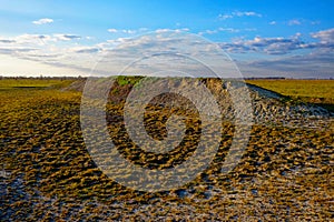 Open field with a large dirt mound, sparse vegetation, and a distant horizon