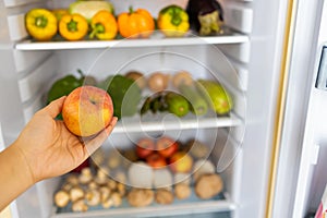 Open fridge full of vegetables and fruits. Woman takes fresh apple from refrigerator.