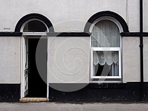 Open front door and window of a typical old brick british terraced house with black and white decorative paintwork