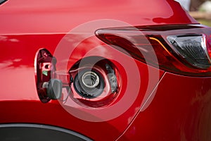 An open fuel tank cap of a red car for filling gasoline or diesel fuel into the gas tank.