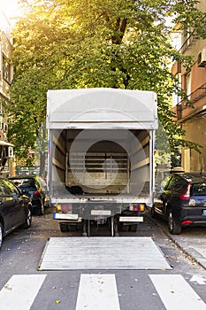 Open furniture delivery truck on a city street. Empty moving van with rear doors opened. On an autumn sunny day