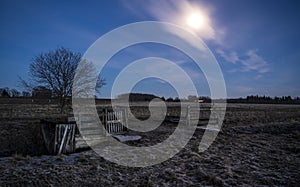 An open gate on a field in the night with a full moon