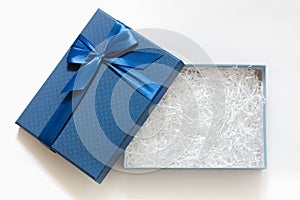 Open gift box with shredded paper on a white background. Blue box with decorative fillers for your product. Flat lay, top view,
