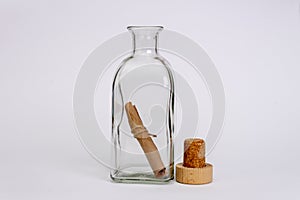 An open glass bottle with an old note inside on a light background, the cork lies next to it. Concept: sea mail, a message from an