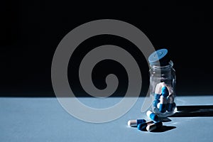 Open glass bottle with scattered antibiotic pills or tablets on a blue table background