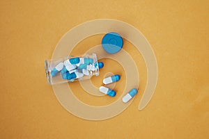 Open glass bottle with scattered antibiotic pills or tablets on a yellow table