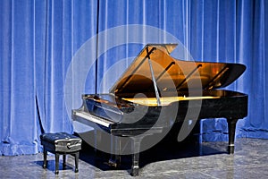 Open grand piano on stage with blue velvet cutain