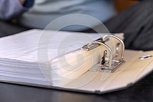 Open gray file folder with metal binder. Papers are on a black desk. Close-up. Selective focus