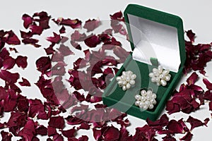An open green velvet box for jewelry. In it lies a set: a ring and earrings with pearls. On a white background, strewn with dried