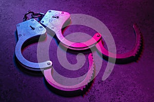 Open handcuffs on a dark background illuminated with a colored mixed light of red and blue