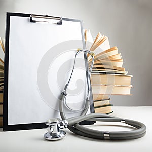 Open hardback books on the table, medical clipboard with blank paper or document, report and stethoscope. Medical