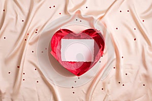 Open heart shaped box with blank paper card mockup inside on beige textile background
