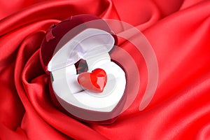 Open heart-shaped gift box with glass heart on red satin fabric background