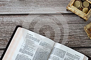 Open holy Bible Book and box with golden coins on a wooden table with copy space, top view