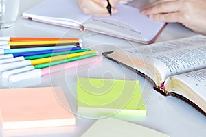 Open holy bible book, colorful notes and markers, and human handwriting in notebook in the background