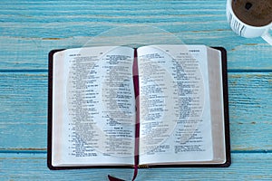 Open Holy Bible Book with cup of coffee on blue wooden backgroun