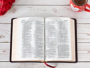 Open Holy Bible Book with a cup of coffee, and red flowers on a wooden table