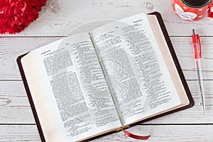 Open Holy Bible Book with fresh red flowers and a cup of a warm coffee cup on a wooden table