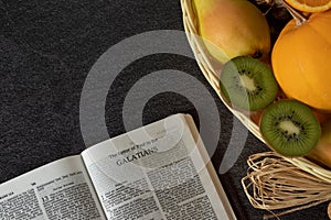 An open Holy Bible book of Galatians with a wicker basket full of various fresh fruits with copy space photo
