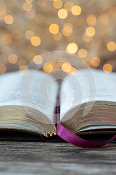 Open holy bible book on wooden table with golden bokeh background, vertical shot