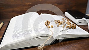 Open Holy Bible With Brown Wooden Beads With Silver Cross On Table